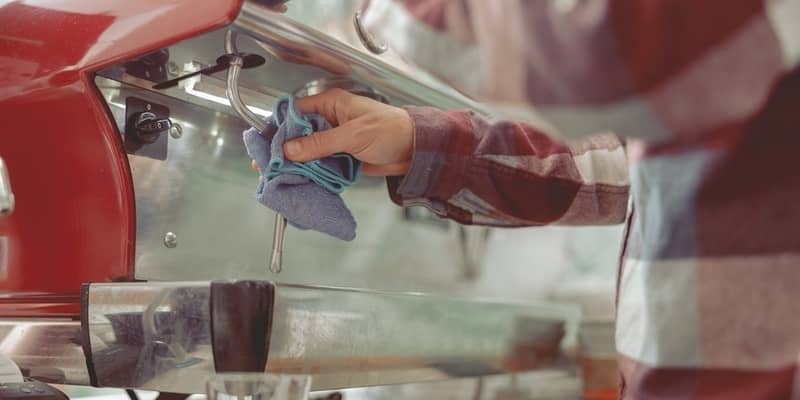 male hand cleaning the steam wand of a coffee machine