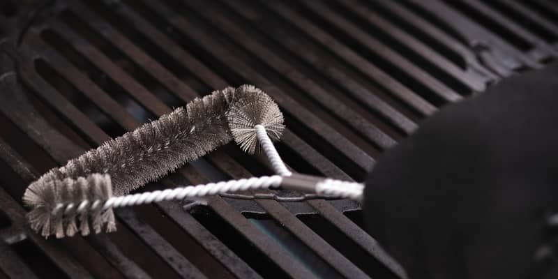 Cleaning outdoor gas grill with a metal brush before next grilling