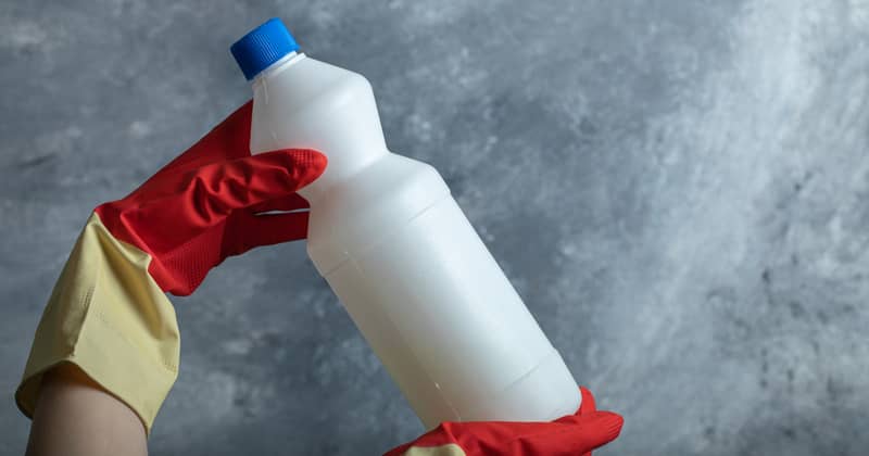 Hands in red gloves holding container of bleach