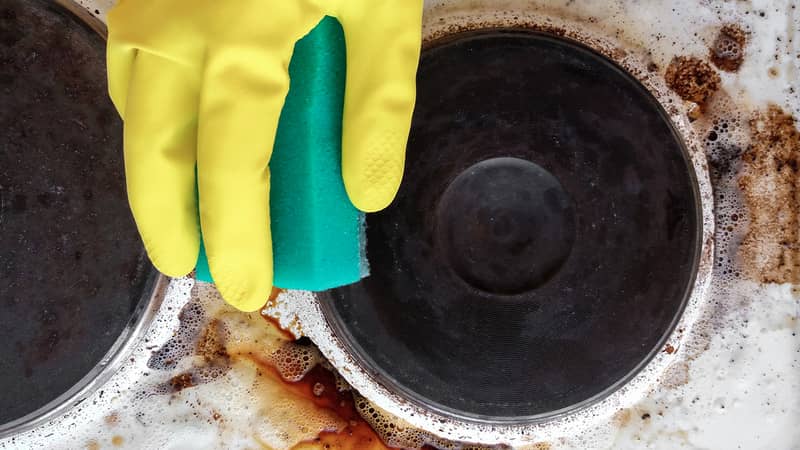 hand in household glove cleaning grease and dirt from kitchen stove