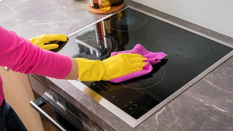 woman with yellow gloves cleaning a glass stove top