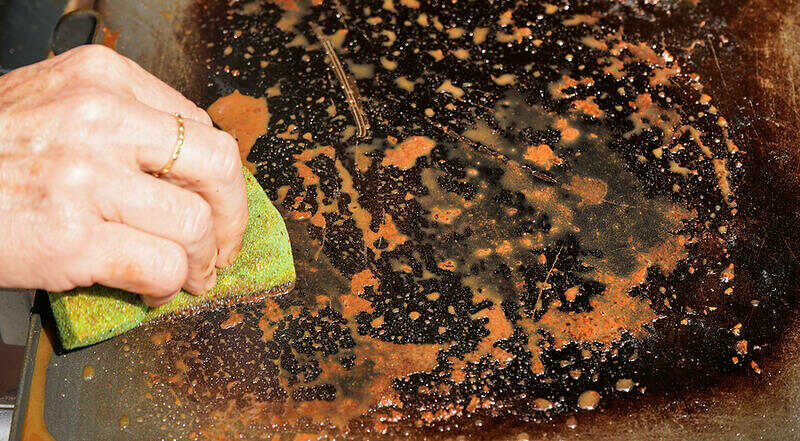 hand holding a sponge cleaning a dirty grill plate