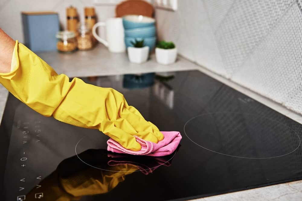 Woman in yellow rubber gloves cleans kitchen induction hob with cloth