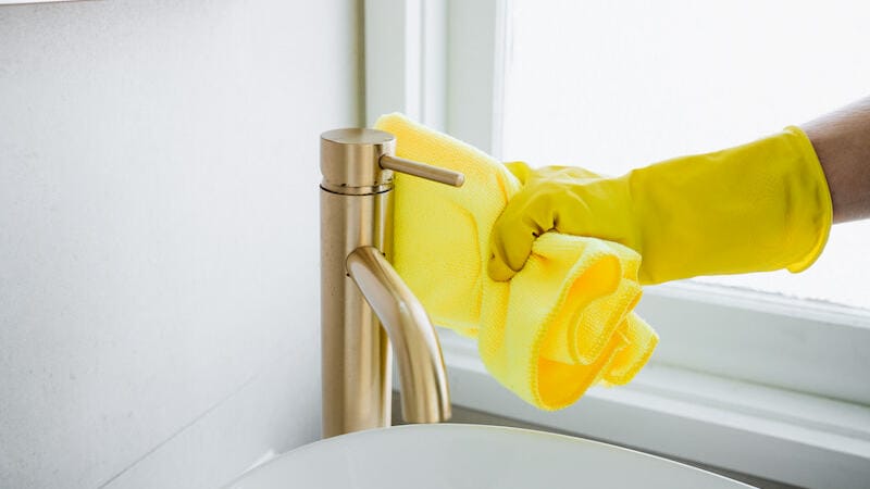A cleaning professional's hand wiping the faucet of the bathroom sink with cloth