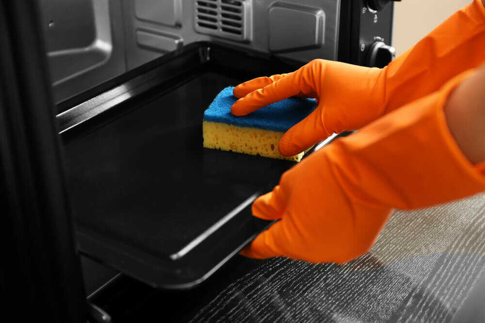 hand with gloves cleaning the oven tray with a sponge