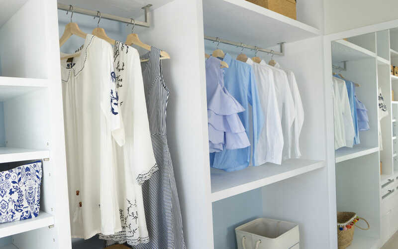 modern wooden wardrobe with women clothes hanging on rail in walk in closet