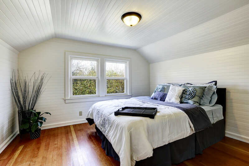 Bedroom with wood plank paneled walls and ceiling. View of black queen size bed and dry branches in the corner