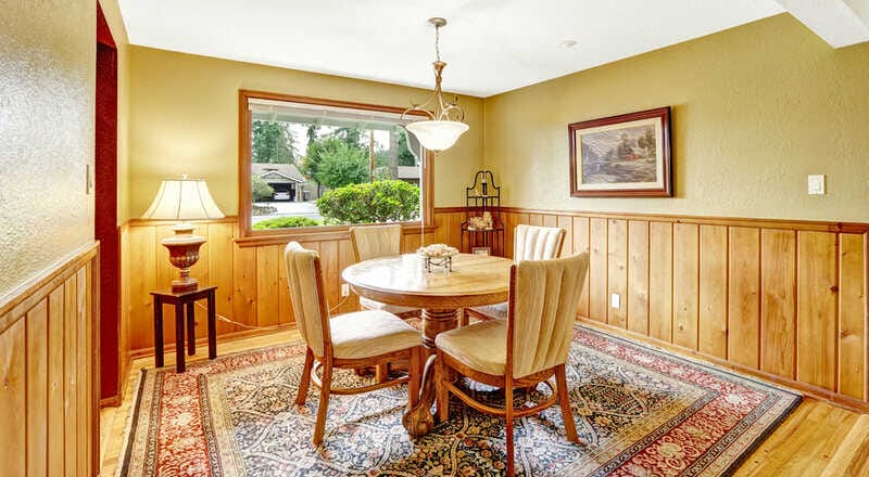 Dining carved wood table set in bright room with plank paneled walls and hardwood floor