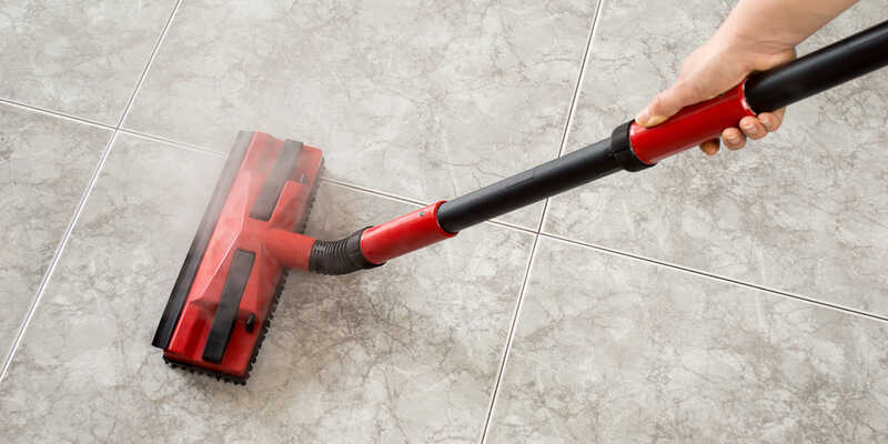 woman using steam mop to clean floor tiles and grout