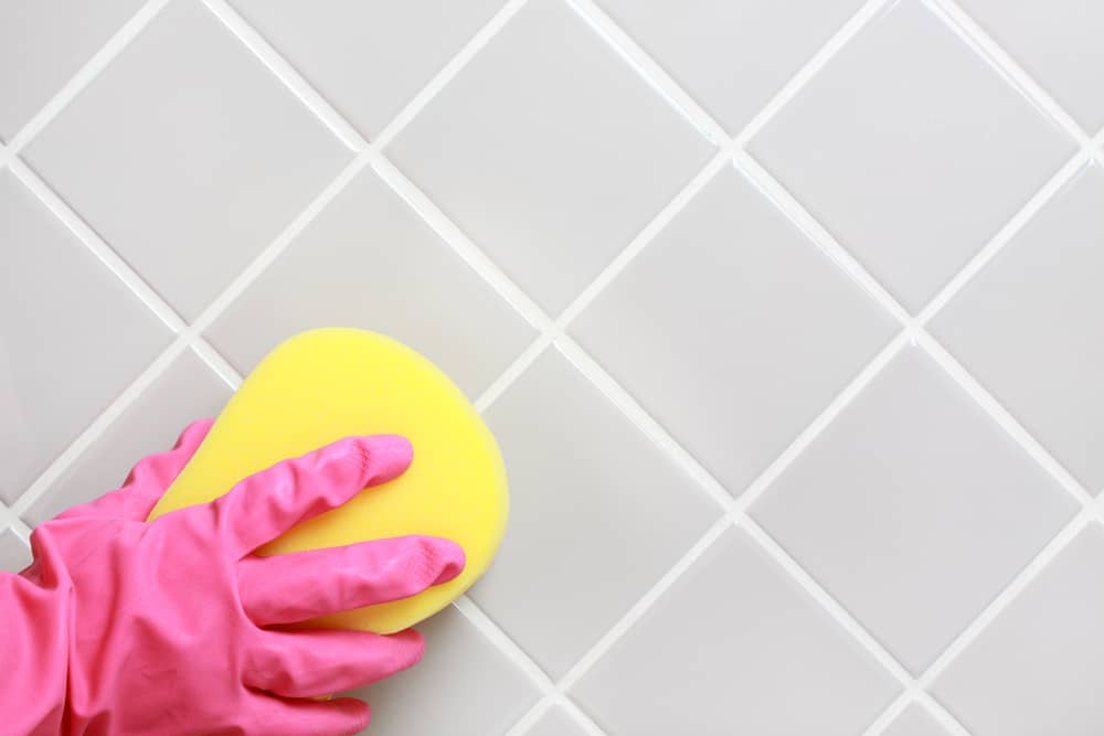 Hand and glove cleaning the bathroom tiles