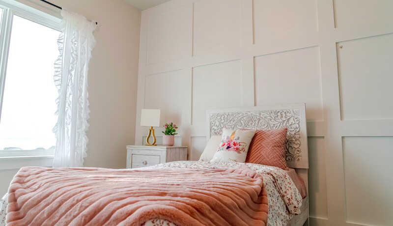 Single bed with decorative headboard and feminine blankets inside a home bedroom.