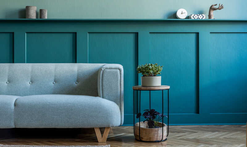 Modern interior of living room with mint sofa, coffee table, plants and elegant decoration. Stylish home decor. Green wooden panelling with shelf and accessories.