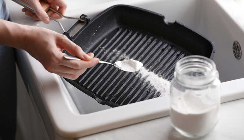 woman uses baking soda as a cleaning agent for the grill pan