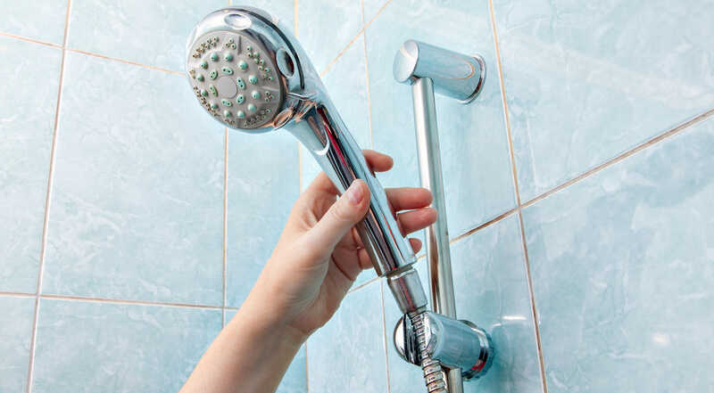 hand holding shower head in a blue bathroom