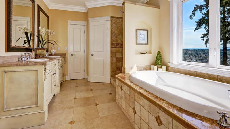 Soft tones bathroom interior with tile floor and tile wall trim, antique vanity with mirror and round bath tub in luxury house