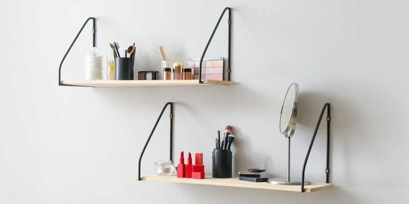 Modern shelves with decorative cosmetics and brushes hanging on light wall
