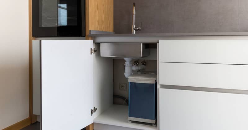 Opened kitchen cabinet with sink and installed garbage bin