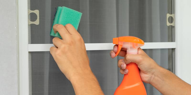 male hands holding sponge and bottle spray, cleaning fixed fly screen