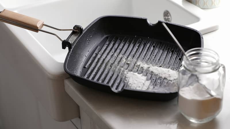 Dirty grill pan and jar with baking soda on countertop near sink in kitchen