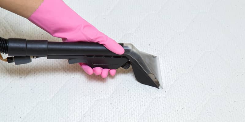 woman hands with pink gloves vacuuming the mattress