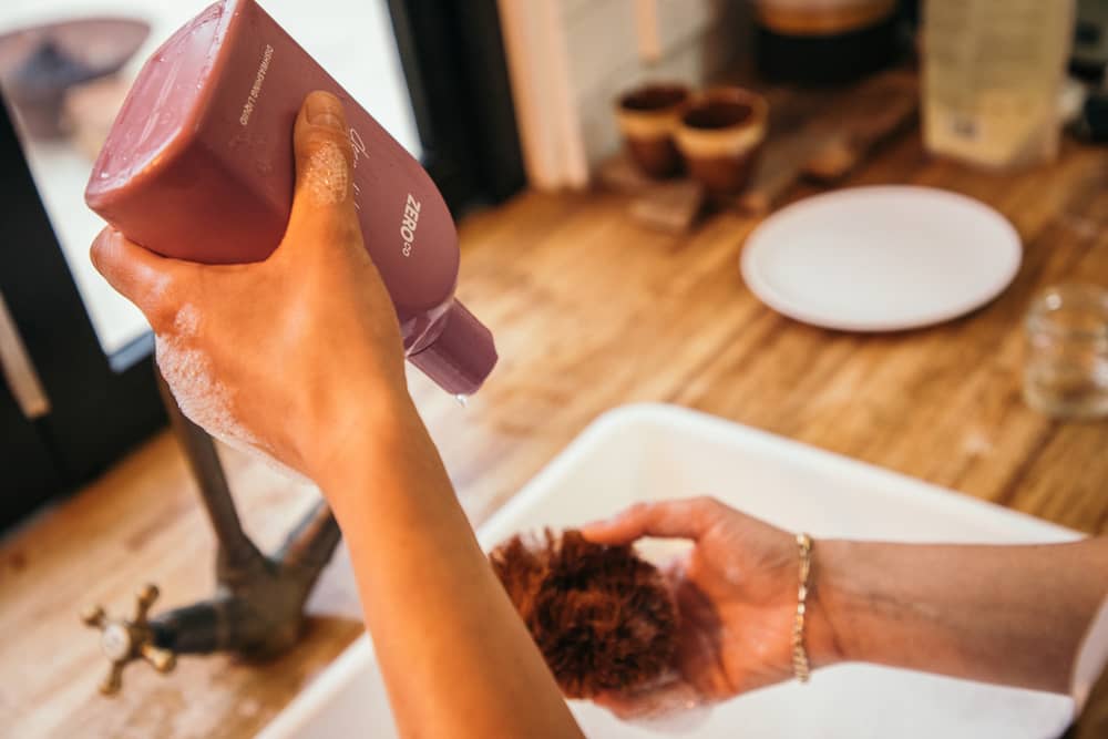 Woman hands using an eco-friendly dishwashing liquid for washing dishes in the kitchen