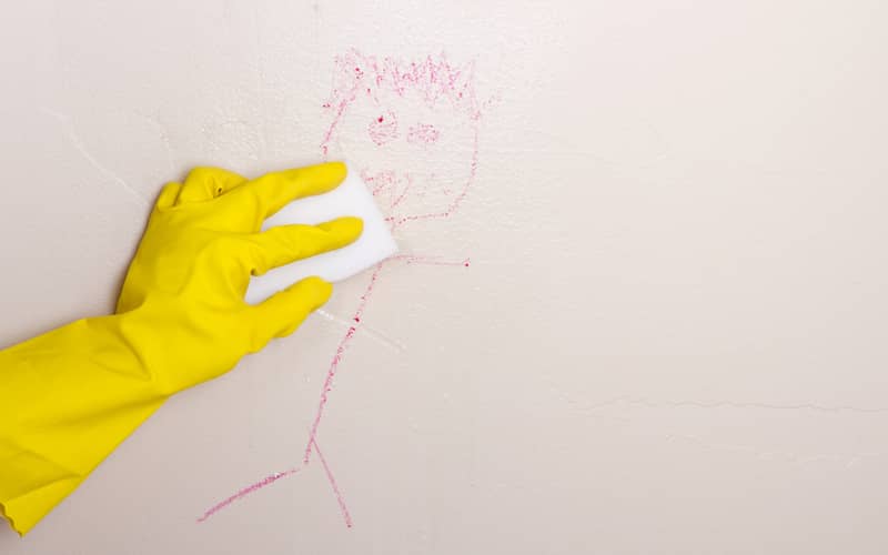 Gloved hand cleaning a drawing made with crayon off of a wall with magic eraser