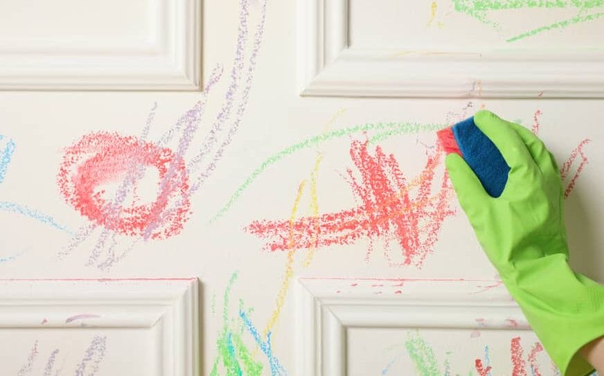 hand wearing gloves using sponge to remove crayon marks off a wall