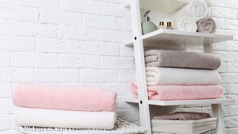 Shelving unit and baskets with clean towels and toiletries near brick wall