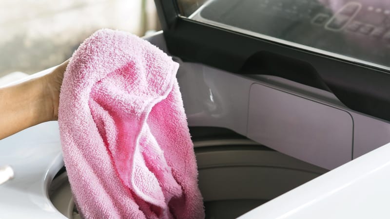 Woman hand holding pink towel to load to the top load washing machine for cleaning.