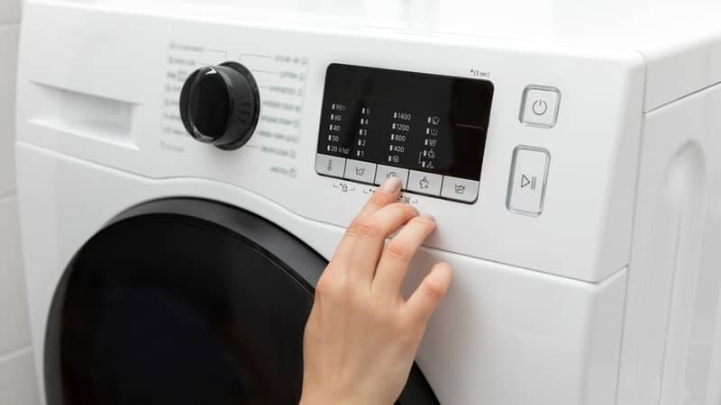 Close-up of a hand selecting a program or function with a finger while pressing on a front load washing machine