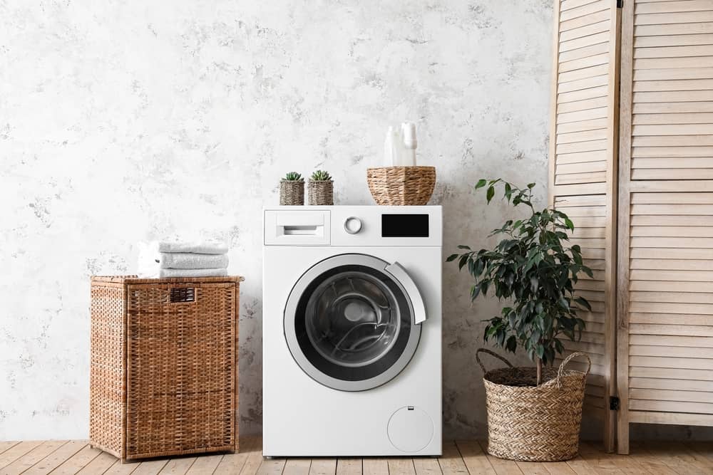 Interior of light laundry room with washing machine, baskets and houseplants