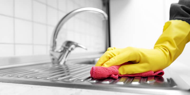 Hands in yellow gloves wiping the kitchen sink.