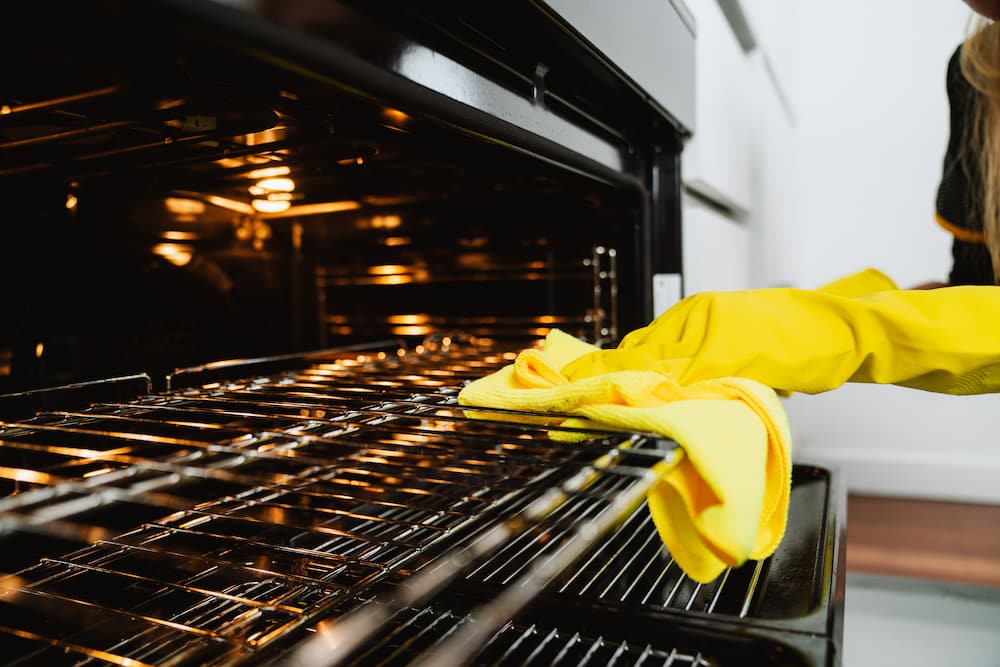 hands in gloves using a cloth to wipe the racks of an oven