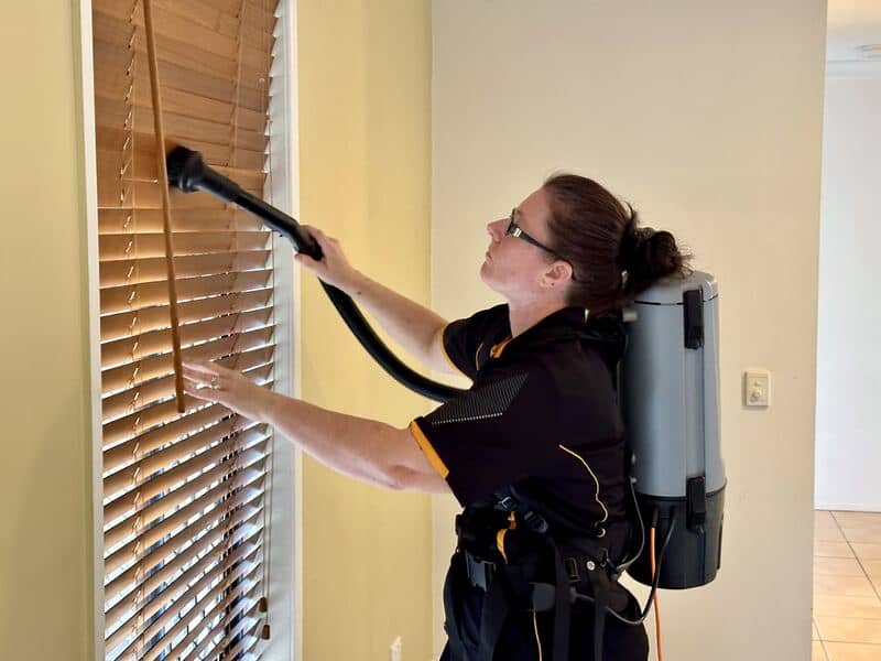 professional cleaner using vacuum to clean blinds