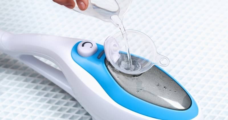 A man pours distilled water into a container of a steam cleaner