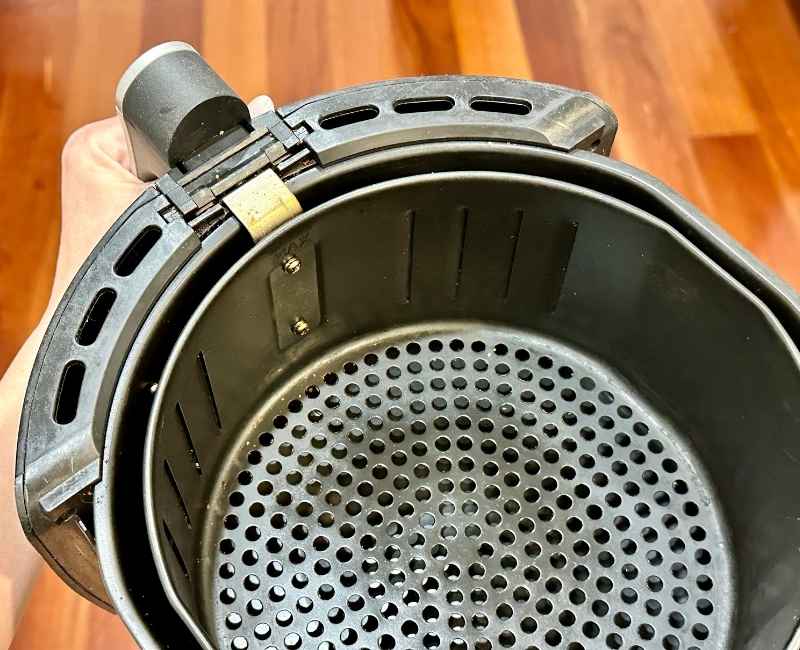 Hand holding an air fryer basket with tray