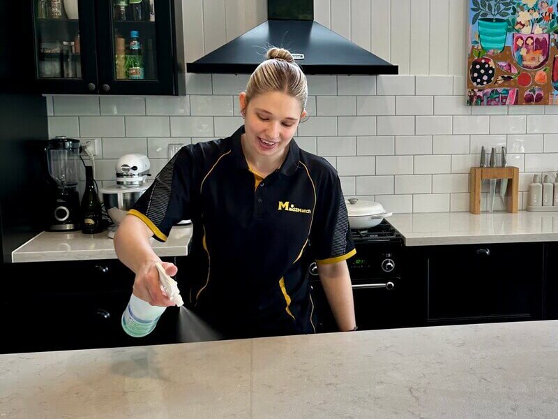 Professional cleaner, Katelyn, disinfecting a stone benchtop