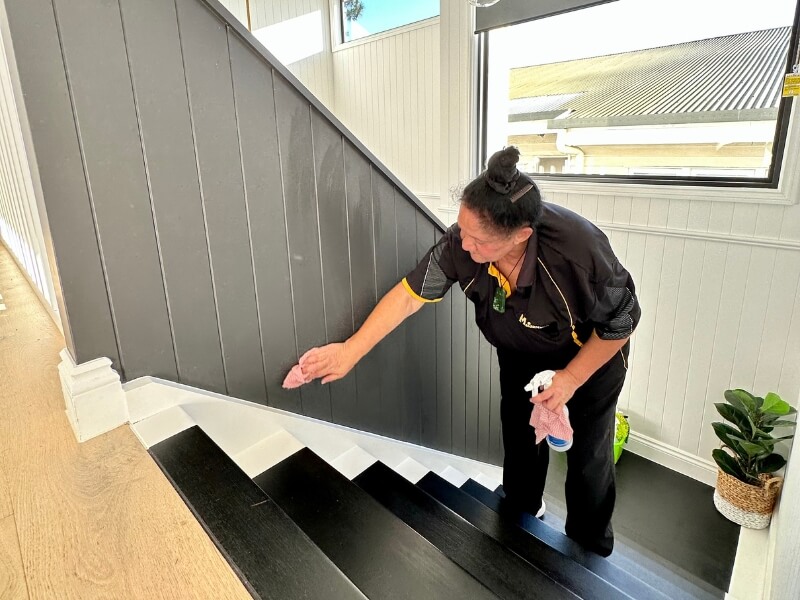 Professional house cleaner wiping the walls on the stairs