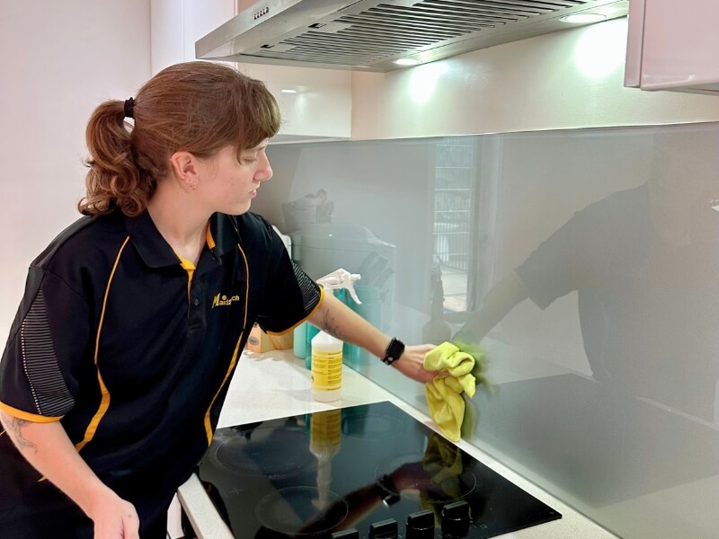 Kayleigh, professional cleaner from Brisbane, wiping the wall behind the stovetop