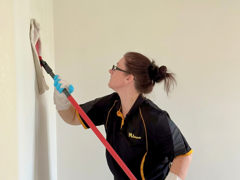 Professional cleaner Renee from Brisbane using a flat mop to thoroughly clean the wall