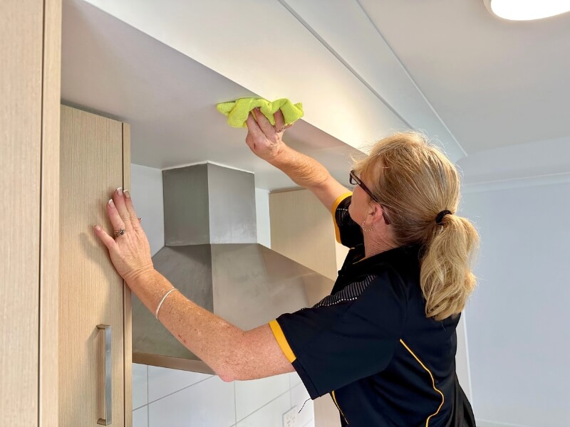 Brisbane professional cleaner Elizabeth cleaning the wall behind the rangehood in the kitchen