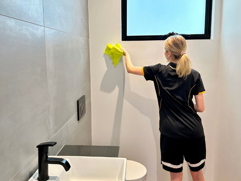 professional cleaner wiping a tiled bathroom wall with a cloth