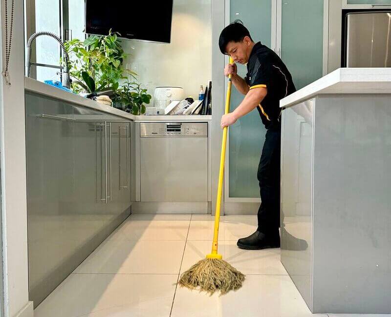 Maid2Match professional cleaner using yellow string mop to mop tiled floors
