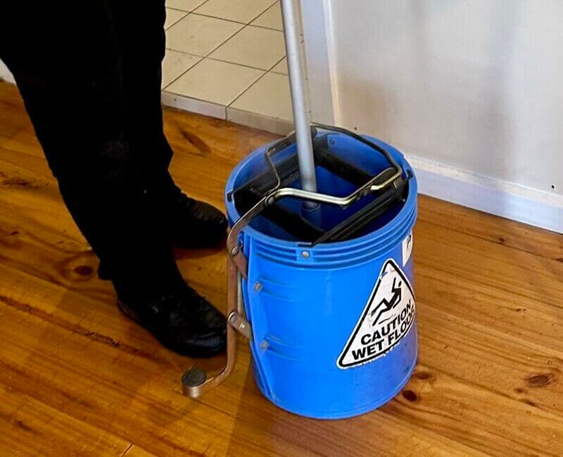 house cleaner dipping a mop into a blue bucket with cleaning solution