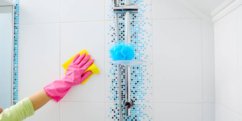 woman hands with pink gloves cleaning shower tiles