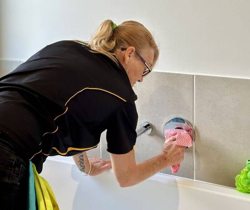 Maid2Match professional cleaner Liz wiping the faucet of the bathtub with a cloth