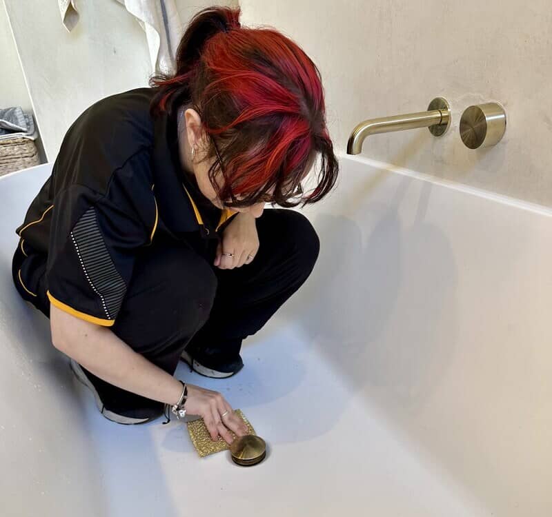 Maid2Match professional cleaner River cleaning the drain of the bathtub with a sponge