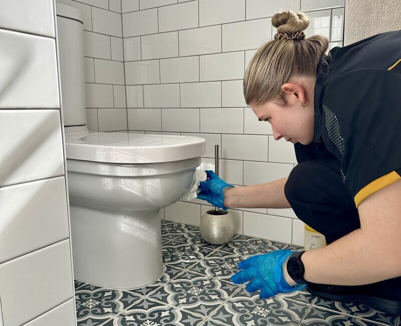 Maid2Match Brisbane professionally trained permanent employee cleaner Kate-lyn cleaning the outside of the toilet
