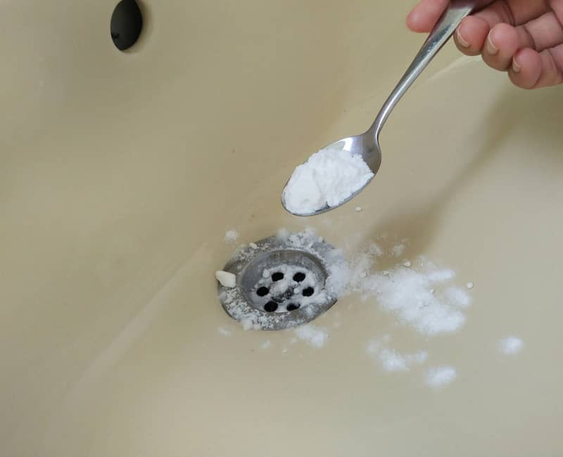 pouring a spoon of bicarb soda in the sink drain
