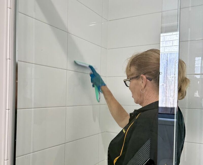 Elizabeth using squeegee to clean shower tiles